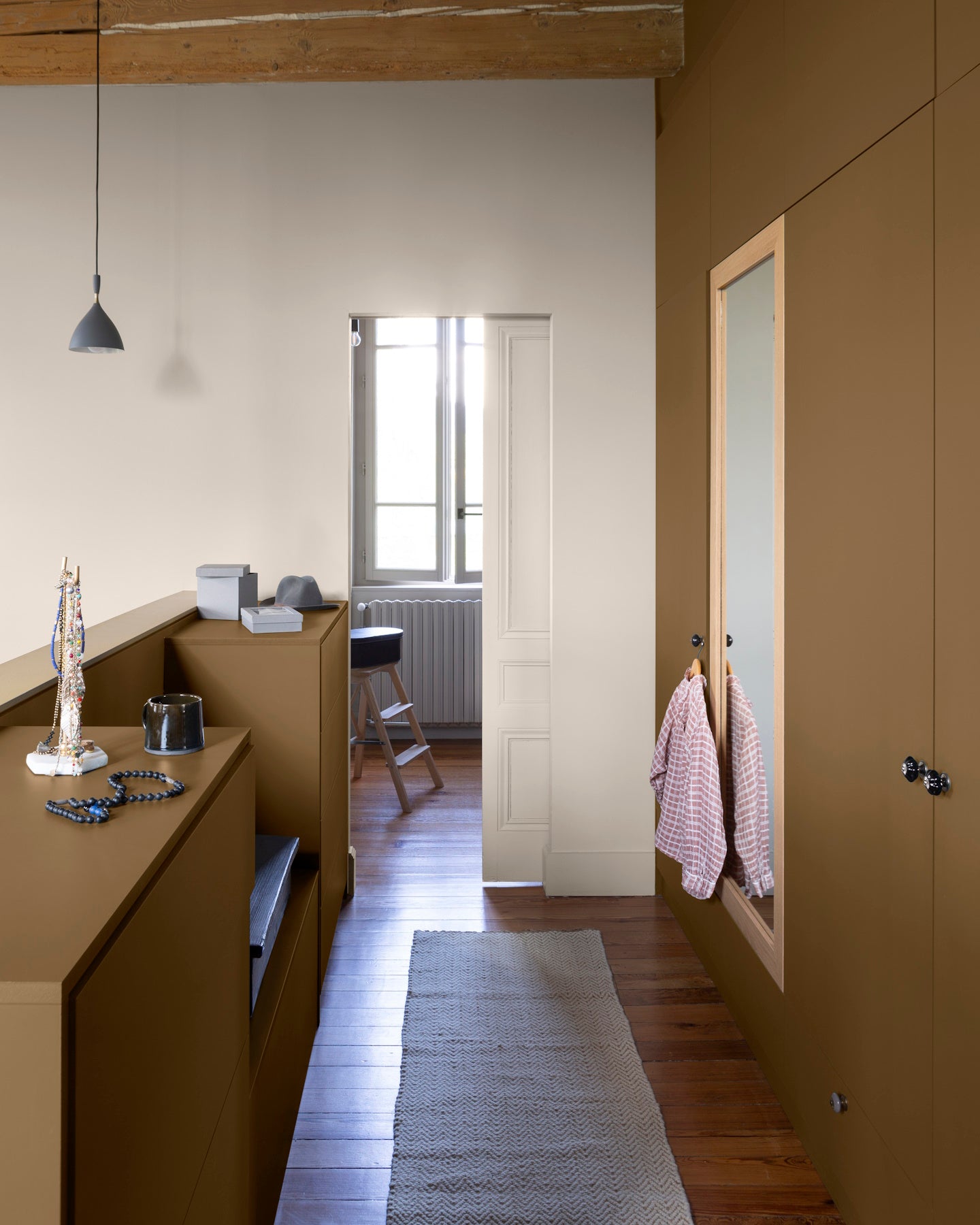 Couloir aux murs bronze astrolabe, Velours de Peinture Libéron, avec bois clair, miroir mural et tapis beige.