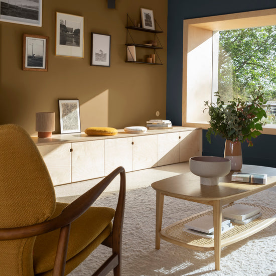 Salon aux murs bronze astrolabe et bleu profond Libéron, avec fauteuil ocre, meuble bas en bois clair et fenêtre.