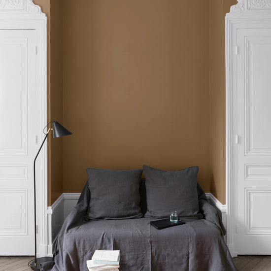 Salon aux murs bronze astrolabe Libéron, avec canapé gris, portes blanches, lampadaire noir et parquet clair.