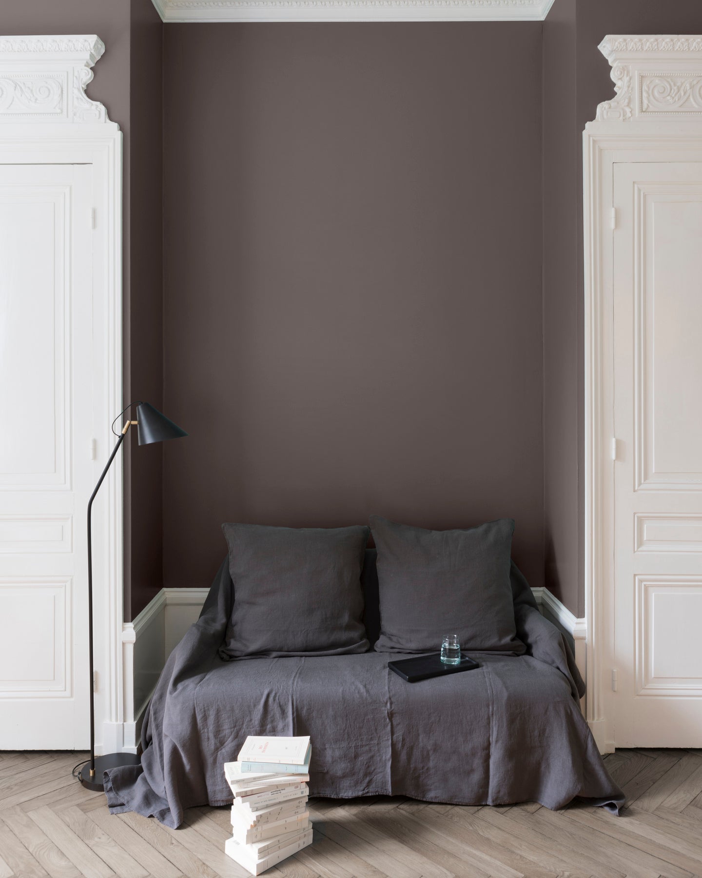 Salon aux murs Brun Minier Velours de Peinture Libéron, avec canapé gris, portes blanches, lampadaire noir et parquet clair.