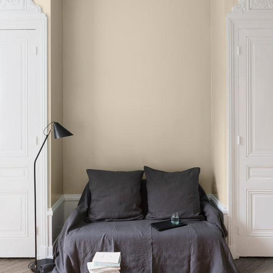 Salon aux murs Camomille Velours de Peinture Libéron, avec canapé gris, portes blanches, lampadaire noir et parquet clair.