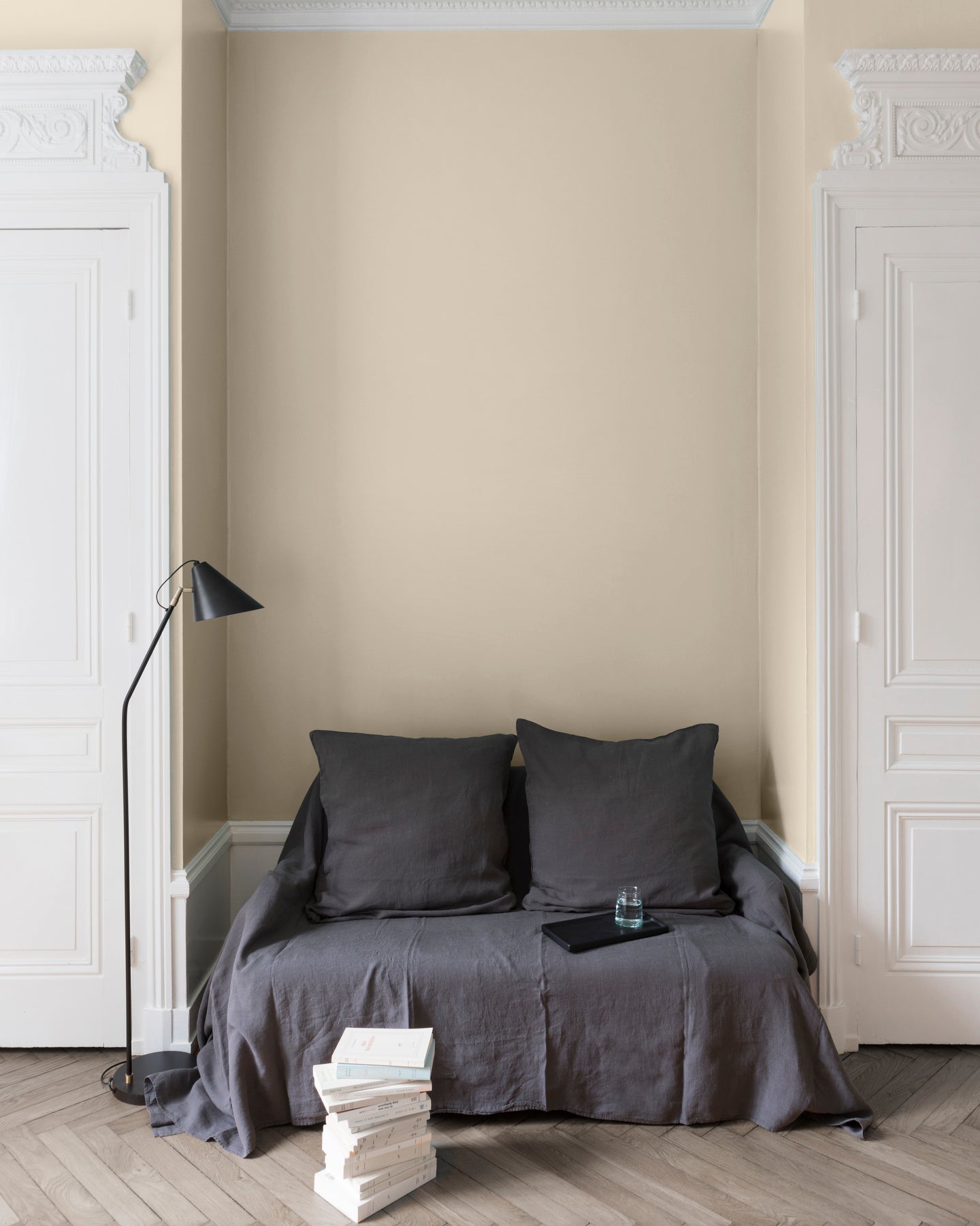 Salon aux murs Camomille Velours de Peinture Libéron, avec canapé gris, portes blanches, lampadaire noir et parquet clair.