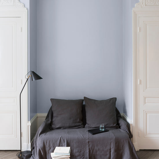 Salon aux murs cap blanc nez Libéron, avec canapé gris, portes blanches, lampadaire noir et parquet clair.