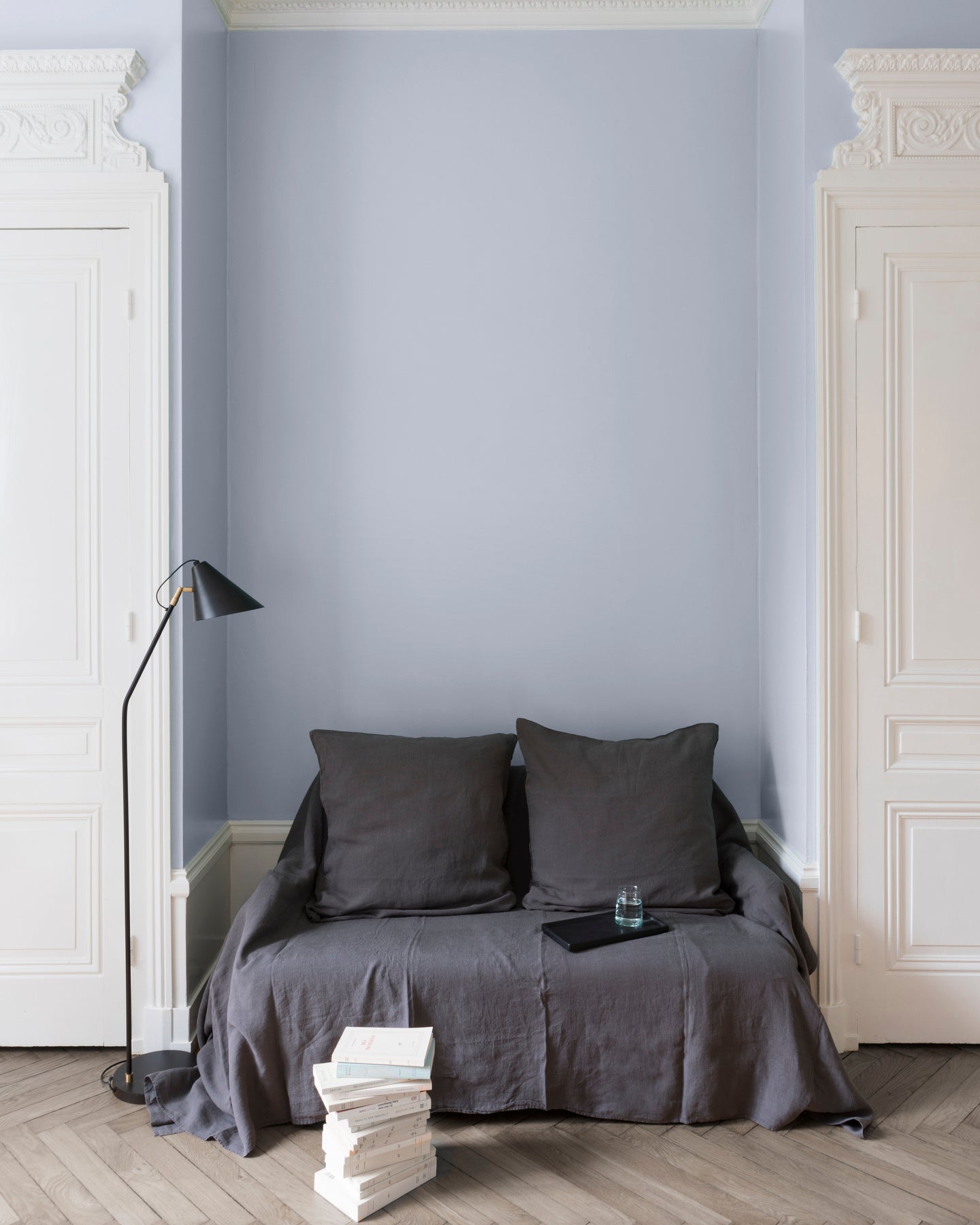 Salon aux murs cap blanc nez Libéron, avec canapé gris, portes blanches, lampadaire noir et parquet clair.