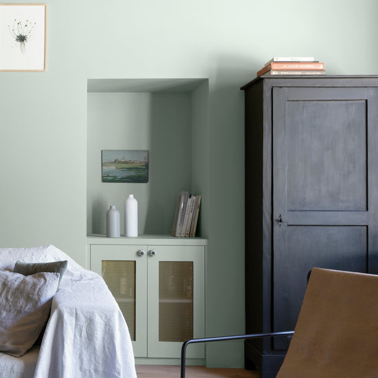 Salon aux murs céladon Libéron, avec niche peinte, meuble noir, fauteuil camel et canapé blanc.