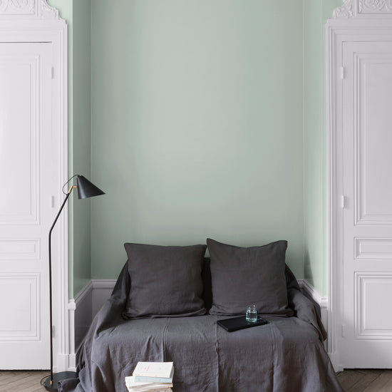 Salon aux murs céladon Libéron, avec canapé gris, portes blanches, lampadaire noir et parquet clair.