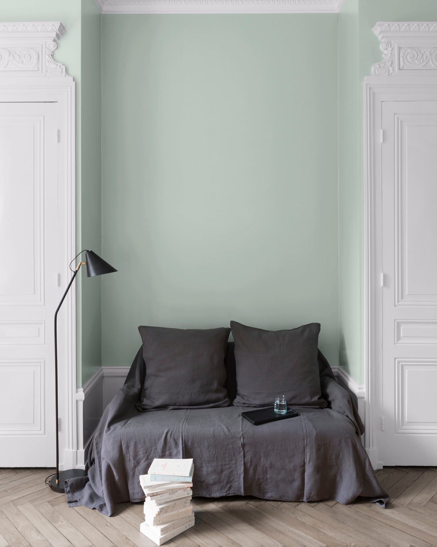 Salon aux murs céladon Libéron, avec canapé gris, portes blanches, lampadaire noir et parquet clair.