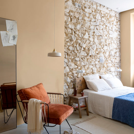 Chambre aux murs confiture de lait, Velours de Peinture Libéron, avec fauteuil terracotta, pierre apparente et linge blanc.