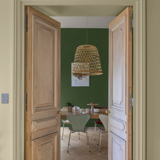 Passage aux murs crème artichaut et vert potager Libéron, avec portes en bois clair et suspension en rotin.