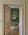 Passage aux murs crème artichaut et vert potager Libéron, avec portes en bois clair et suspension en rotin.