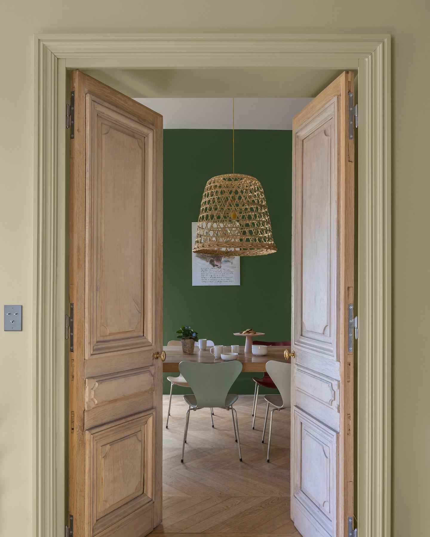 Passage aux murs crème artichaut et vert potager Libéron, avec portes en bois clair et suspension en rotin.