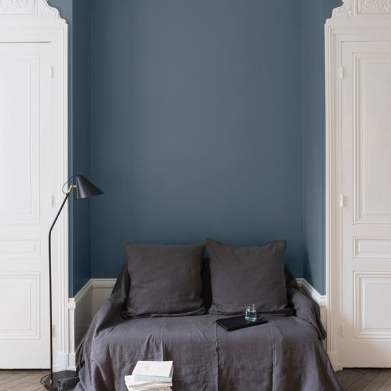 Salon aux murs Fine de Claire Velours de Peinture Libéron, avec canapé gris, portes blanches, lampadaire noir et parquet clair.
