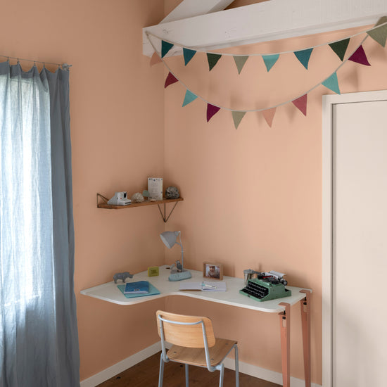 Chambre aux murs grès rosé, Velours de Peinture Libéron, avec bureau blanc, chaise en bois et guirlande colorée.