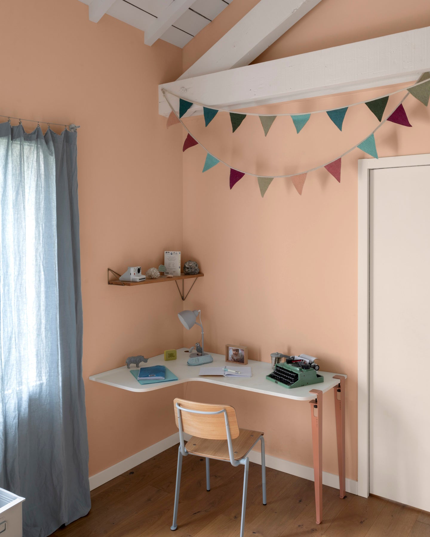 Chambre aux murs grès rosé, Velours de Peinture Libéron, avec bureau blanc, chaise en bois et guirlande colorée.