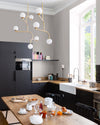 Cuisine aux murs gris sarrazin et blanc Meudon Libéron, avec meubles noirs, table en bois et suspension dorée.