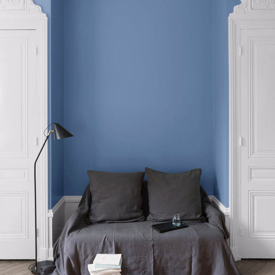 Salon aux murs Heure Bleue, Velours de Peinture Libéron, avec canapé gris, portes blanches et parquet clair.