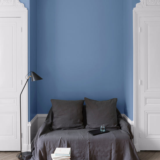 Salon aux murs heure bleue Libéron, avec canapé gris, portes blanches, lampadaire noir et parquet clair.