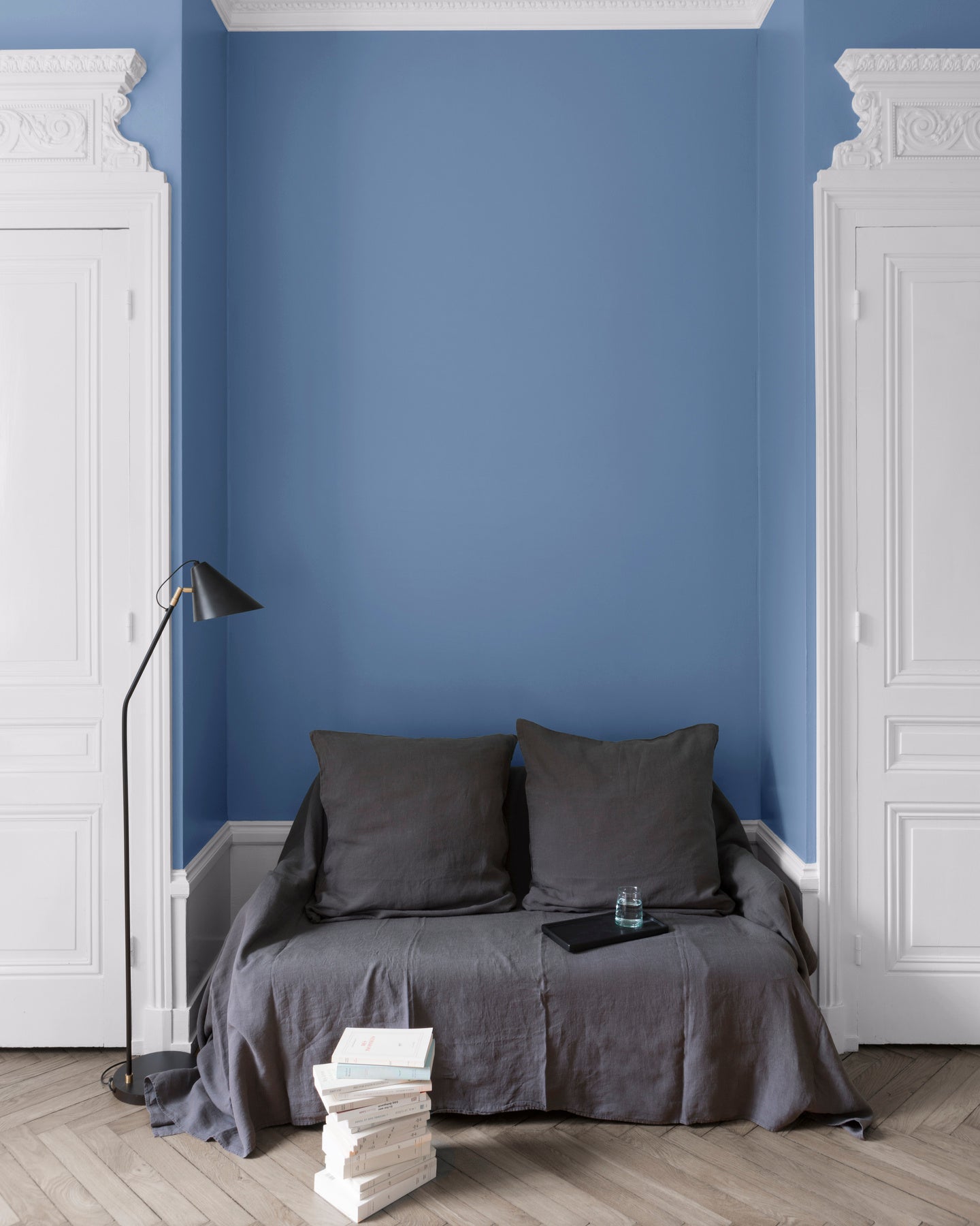 Salon aux murs heure bleue Libéron, avec canapé gris, portes blanches, lampadaire noir et parquet clair.