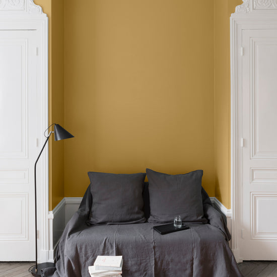Salon aux murs jaune calisson Libéron, avec canapé gris, portes blanches, lampadaire noir et parquet clair.