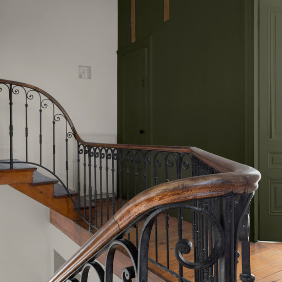 Cage d’escalier aux murs kaki barda et gris peurotte Libéron, avec rampe en fer forgé et marches en bois.