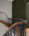 Cage d’escalier aux murs kaki barda et gris peurotte Libéron, avec rampe en fer forgé et marches en bois.
