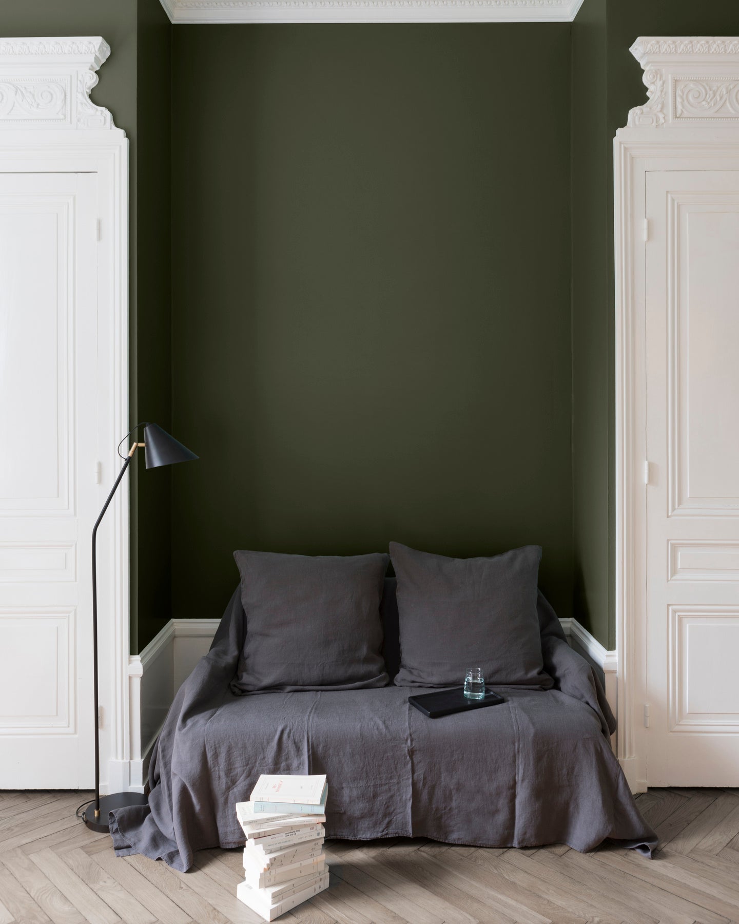 Salon aux murs kaki barda Libéron, avec canapé gris, portes blanches, lampadaire noir et parquet clair.