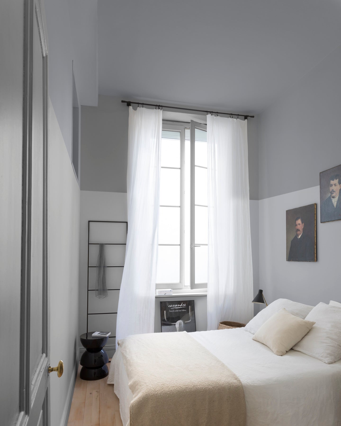 Chambre aux murs lumière opale et gris Gustave Libéron, avec lit blanc, rideaux légers et portraits encadrés.