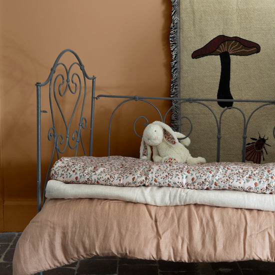 Chambre d’enfant aux murs ocre de Broux Libéron, avec lit en fer gris, linge rose poudré et lapin en peluche.