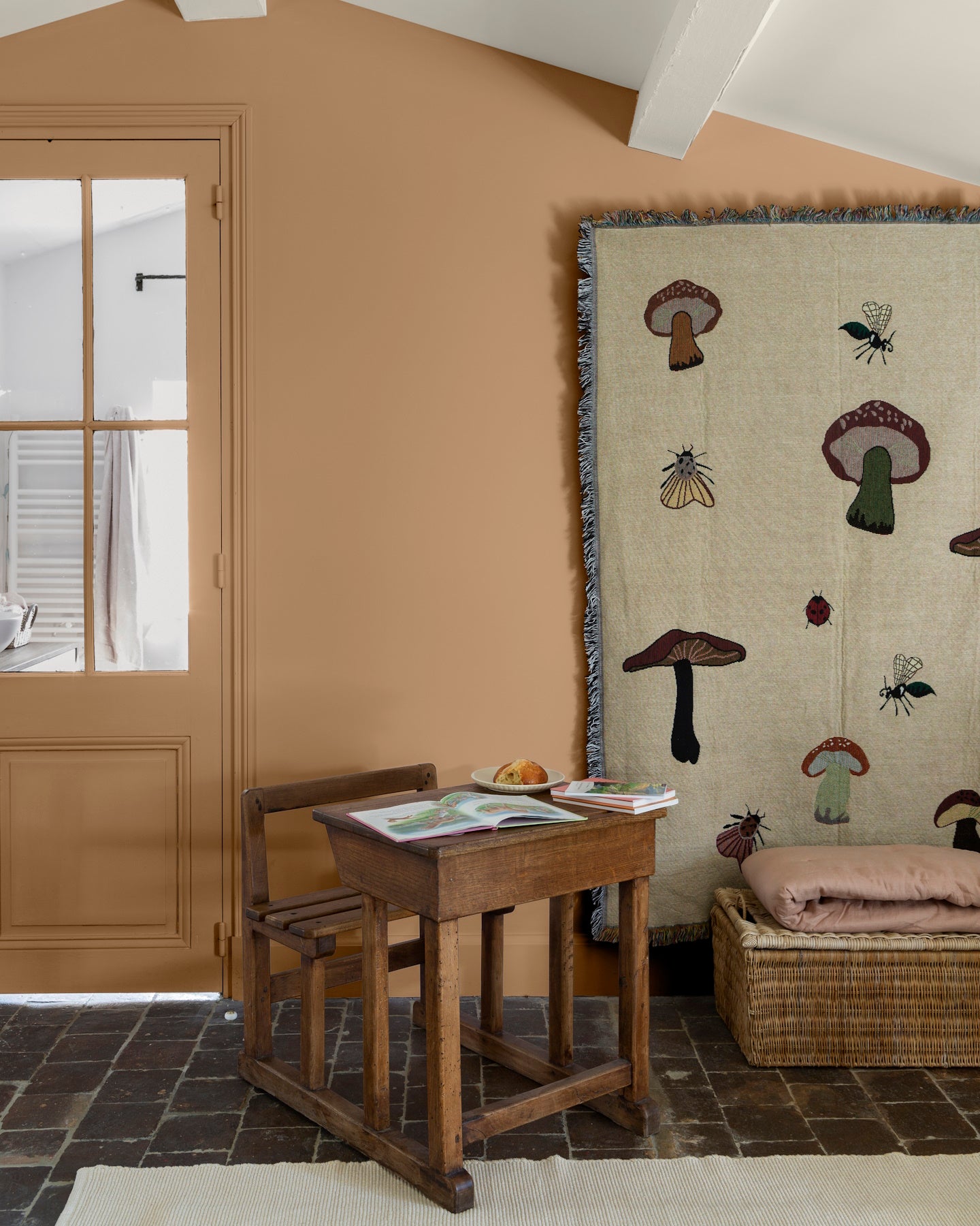 Pièce aux murs ocre Bruoux, Velours de Peinture Libéron, avec porte peinte, petit bureau en bois et tapisserie décorative.
