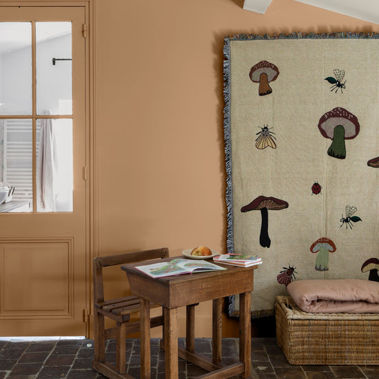 Coin enfant aux murs ocre de Broux Libéron, avec pupitre en bois, porte vitrée et grand tapis illustré.