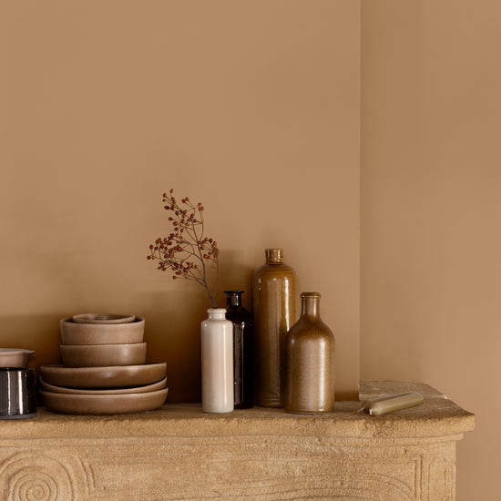 Détail de cheminée aux murs ocre de Broux Libéron, avec vaisselle beige et flacons décoratifs.
