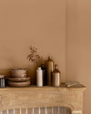 Détail de cheminée aux murs ocre de Broux Libéron, avec vaisselle beige et flacons décoratifs.