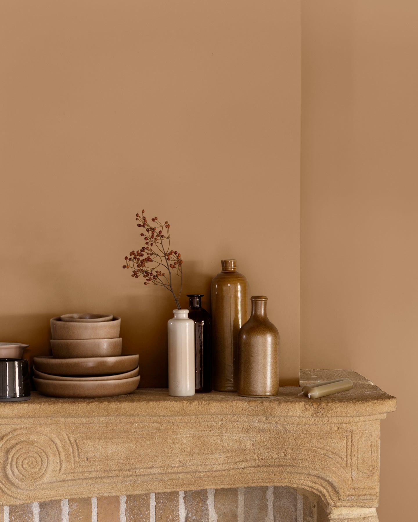 Détail de cheminée aux murs ocre de Broux Libéron, avec vaisselle beige et flacons décoratifs.