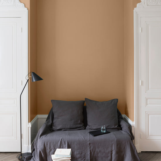 Salon aux murs Ocre de Bruoux, Velours de Peinture Libéron, avec canapé gris, portes blanches et parquet clair.