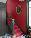 Cage d’escalier aux murs rouge Odéon et gris gravure Libéron, avec portrait ovale, escalier noir et tapis rouge.