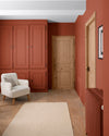Pièce aux murs roux goupil, Velours de Peinture Libéron, avec placard peint, portes en bois et fauteuil crème.