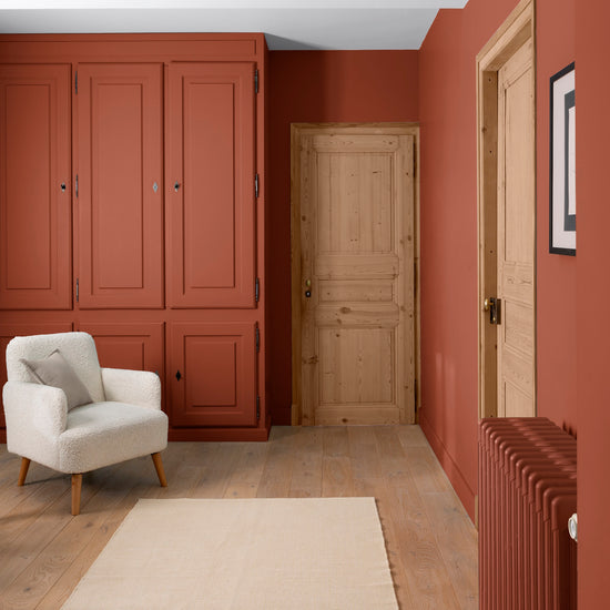 Pièce aux murs roux goupil Libéron, avec placard assorti, porte en bois clair, fauteuil écru et tapis beige.