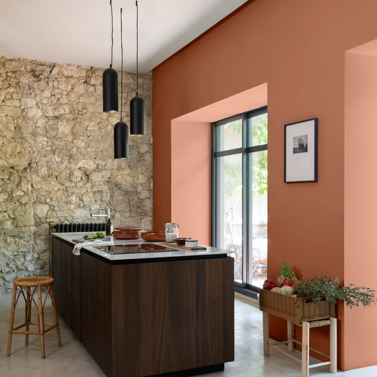 Cuisine lumineuse avec un mur en pierre, et murs oranges, peinture Velours de Peinture Terre Cuite d'Anjou Libéron, et îlot central en bois
