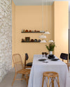Salle à manger aux murs vanille bourbon, Velours de Peinture Libéron, avec chaises en rotin, table blanche et pierre apparente.