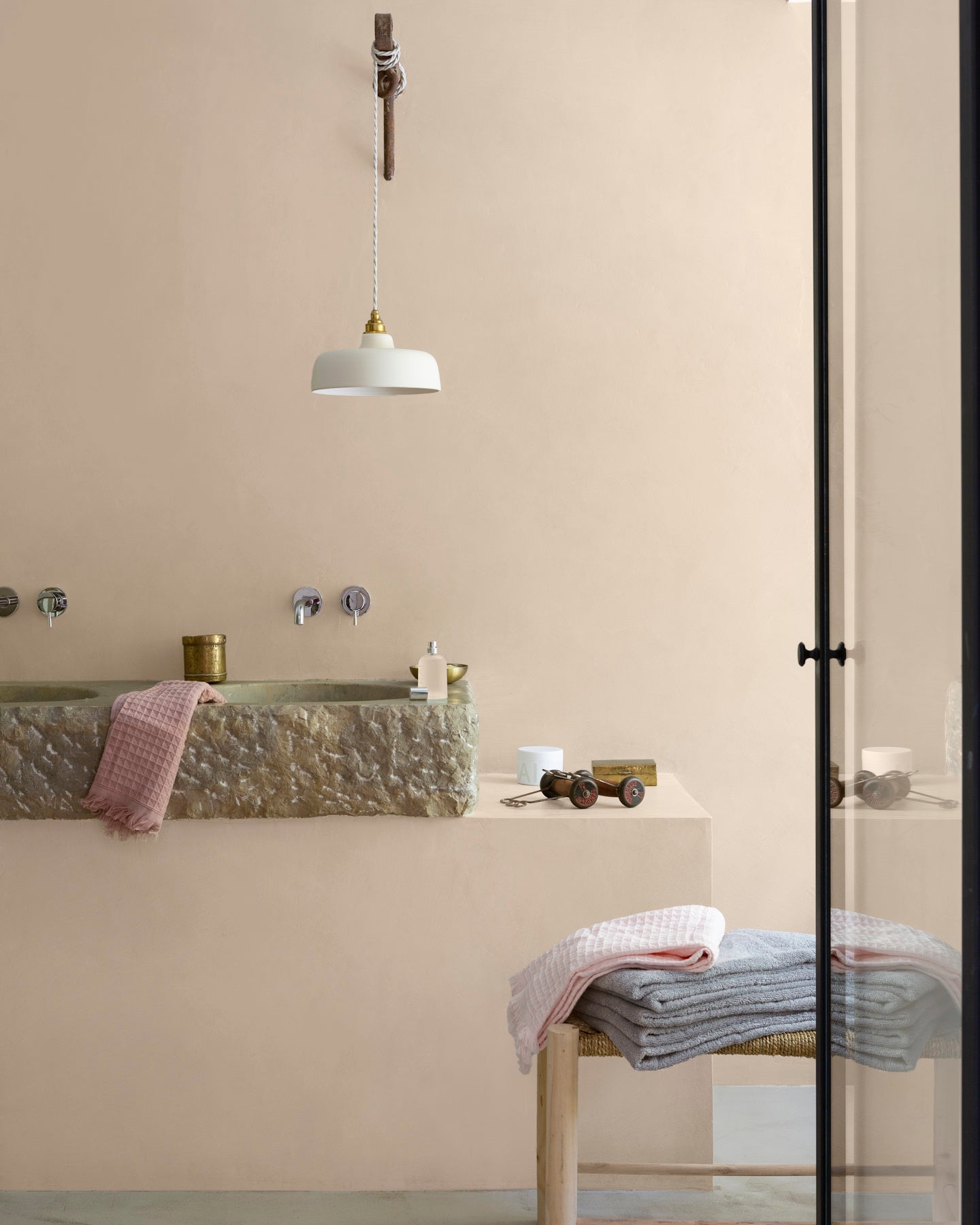 Salle de bain aux murs vélin, Velours de Peinture Libéron, avec vasque en pierre, suspension blanche et linge pastel.
