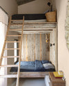 Chambre cabine aux murs vélin Libéron, avec lits superposés en bois brut, échelle, linge bleu et panier en osier.