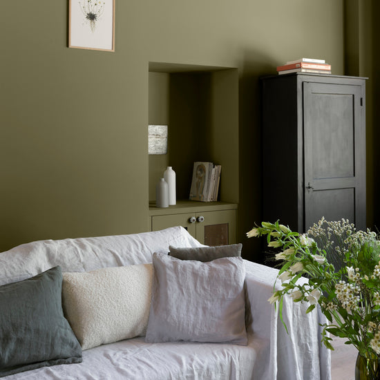 Salon aux murs vert bocage Libéron, avec canapé blanc, niche peinte, meuble noir et bouquet de fleurs.