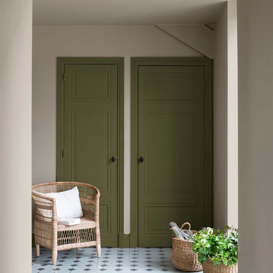 Entrée aux portes vert bocage et murs beige quai de Seine Libéron, avec fauteuil en rotin et paniers tressés.