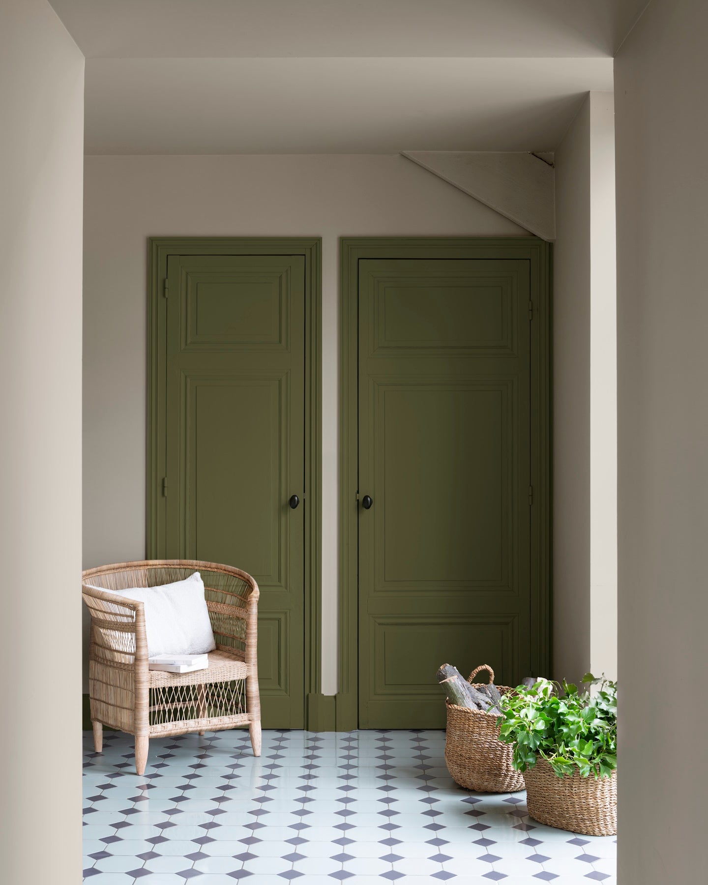 Entrée aux portes vert bocage et murs beige quai de Seine Libéron, avec fauteuil en rotin et paniers tressés.
