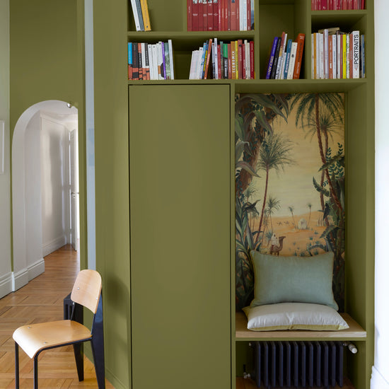 Bibliothèque peinte vert herbarium Libéron, avec étagères intégrées, niche décorative et chaise en bois clair.