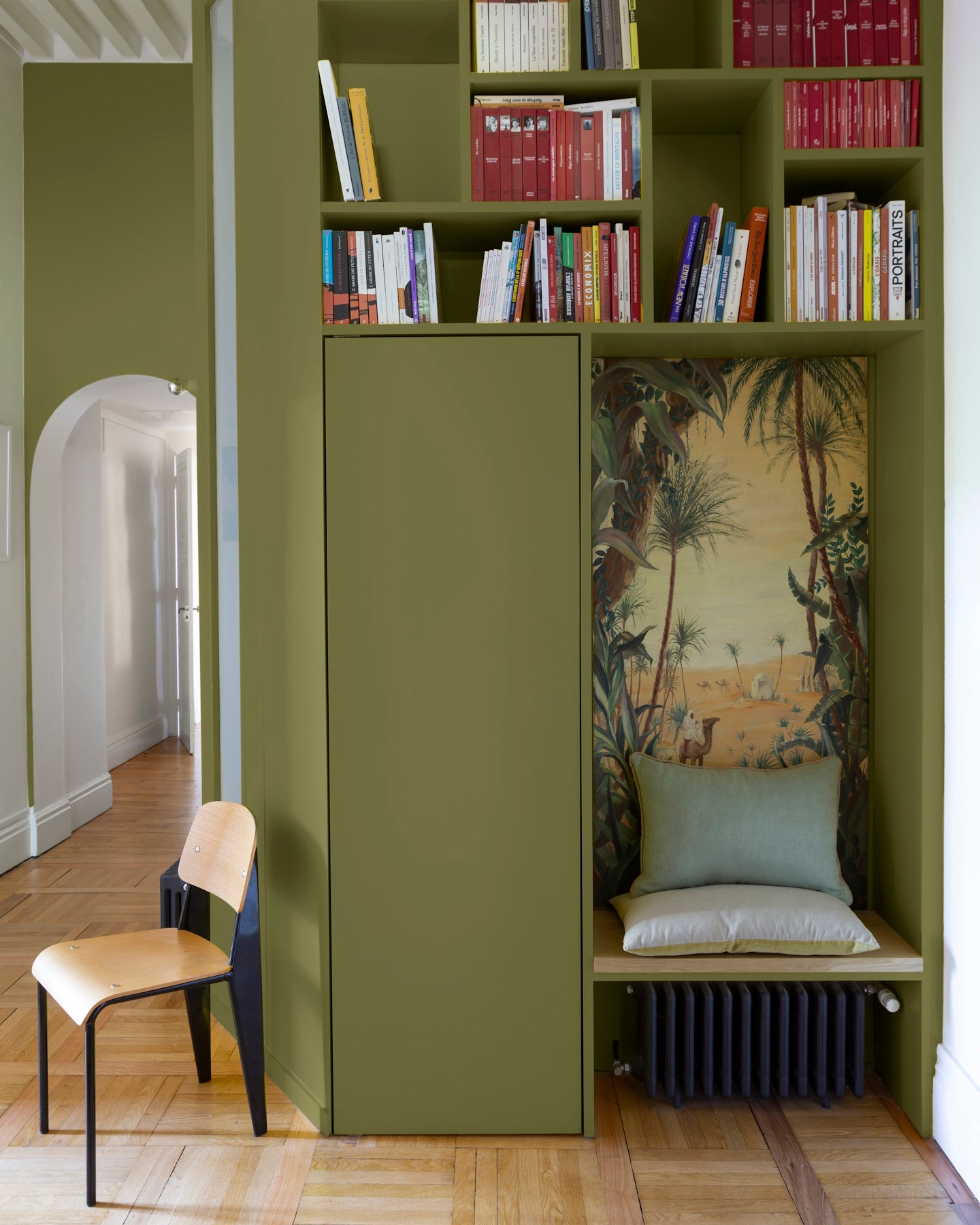 Bibliothèque peinte vert herbarium Libéron, avec étagères intégrées, niche décorative et chaise en bois clair.