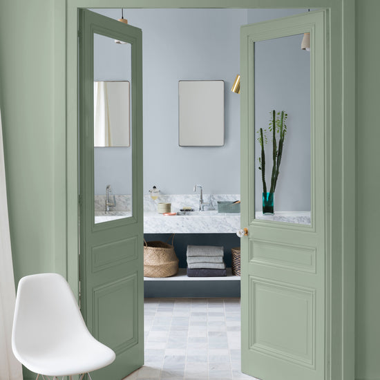 Salle de bain aux murs vert Luxembourg et petit bleu Libéron, avec portes vitrées vertes, chaise blanche et meuble vasque.