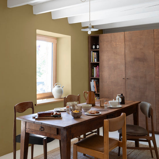 Salle à manger avec une table et des chaises en bois, un tapis en fibres naturelles, un grand meuble de rangement et des murs peints avec la peinture Libéron Velours de Peinture, teinte Vert Picholine.   