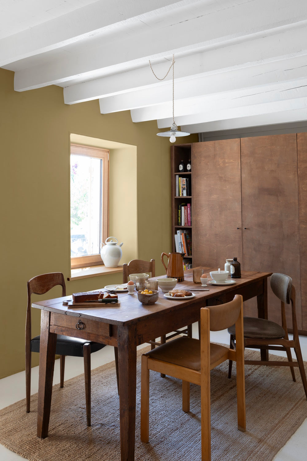 Salle à manger avec une table et des chaises en bois, un tapis en fibres naturelles, un grand meuble de rangement et des murs peints avec la peinture Libéron Velours de Peinture, teinte Vert Picholine.   