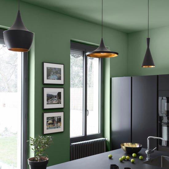 Cuisine ambiance moderne avec murs verts, peinture Velours de Peinture Vert Potager Libéron, avec cadres sur les murs, meubles, luminaires et électroménagers noirs.